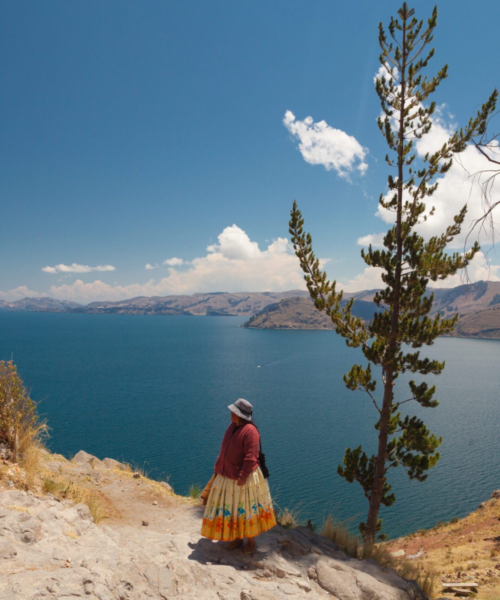 Two Women In Traditional Bolivian Clothes Standing On The Rock Close To The Titicaca Lake.